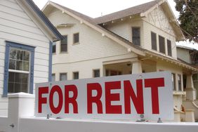For Rent sign in front of a small white house with blue trim.