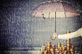 Man holding an umbrella over a stack of coins to give protection of assets from rain