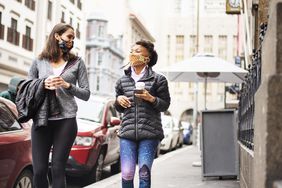 Two women walk down city street drinking coffee