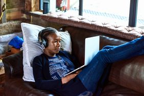 person with headphones sitting on the couch with feet up using a computer