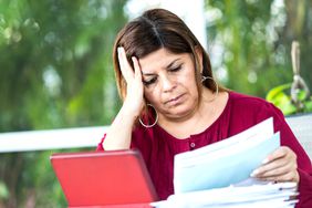 Frowning woman resting her head on her hand, looking at bills and a laptop