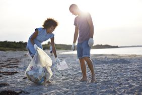 two people standing on a beach picking up trash and putting it into the plastic bag