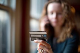 Woman's Hand Holding a Credit Card With Her Unfocused Image in Background, Holding Cellphone