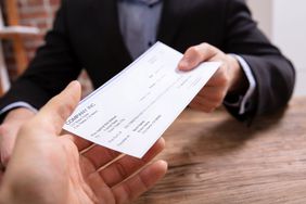 Hand of man in a dark suit handing a check to another person's open hand across a desk