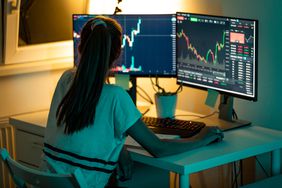 Woman consults two computer monitors with stock graphs