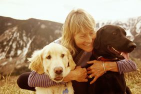 Mature woman hugs her two dogs in the mountains