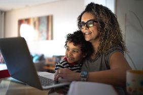 Woman in glasses uses laptop with young son in lap