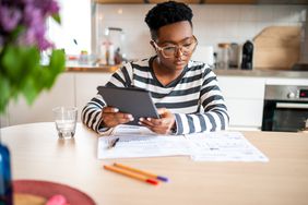 Woman sitting at table holds digital tablet while reviewing paperwork