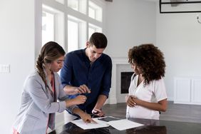 Real estate agent and couple signing documents in new home 