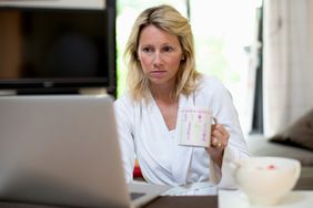 Woman checking laptop with cup of coffee in hand